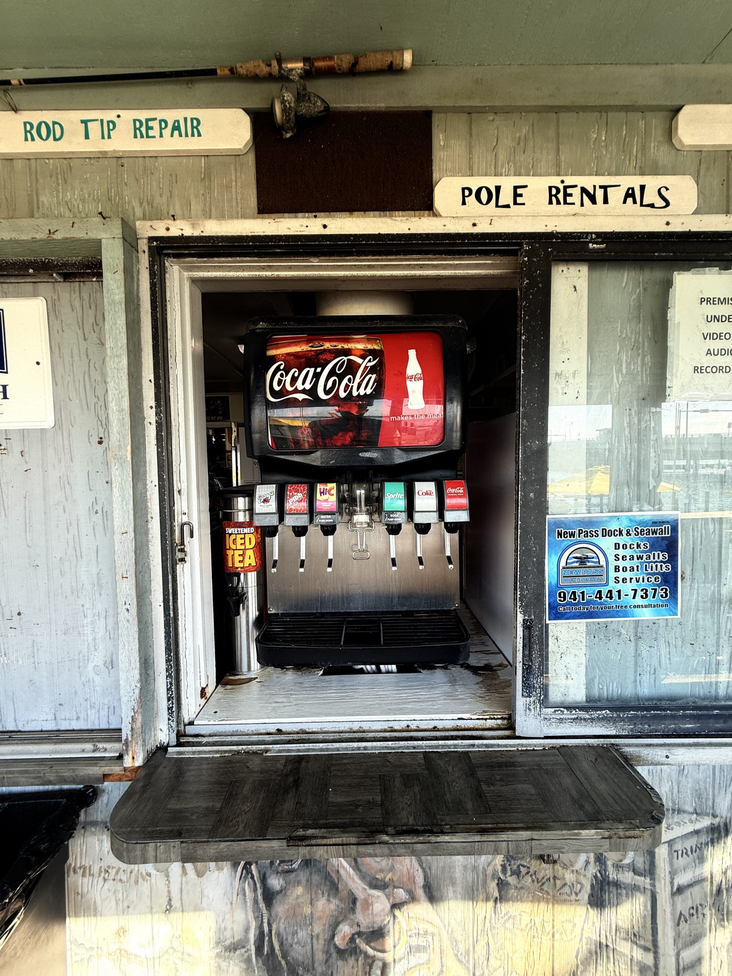 The New Pass bait shop entrance with the pole rentals sign and a cold-drink cooler